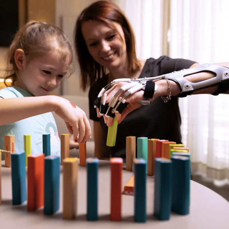 Frau mit DAHO Handorthese spielt Domino mit Kind – alltagsnahe Unterstützung und Bewegungsförderung 