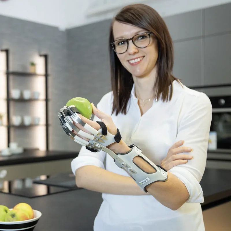 Frau mit Handorthese hält Apfel in der Küche – funktionelle Unterstützung und Beweglichkeit im Alltag mit DAHO